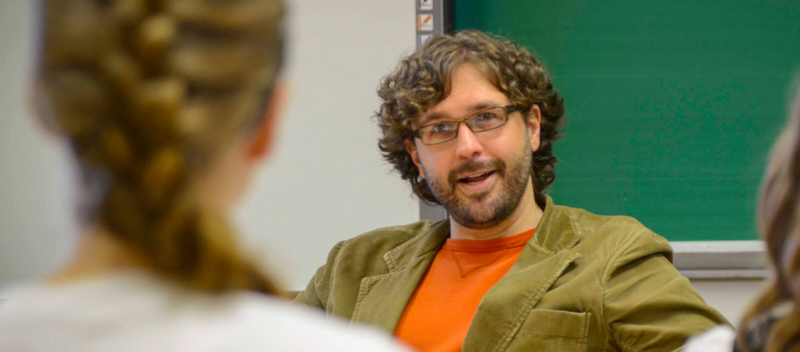 Professor Joel Mann sitting in a desk in the classroom