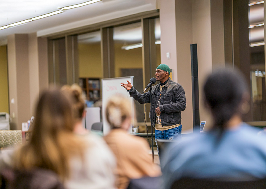 Man speaking at microphone in front of audience in the Mulva Library.