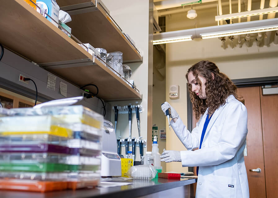 Student in white lab coat working in biology lab