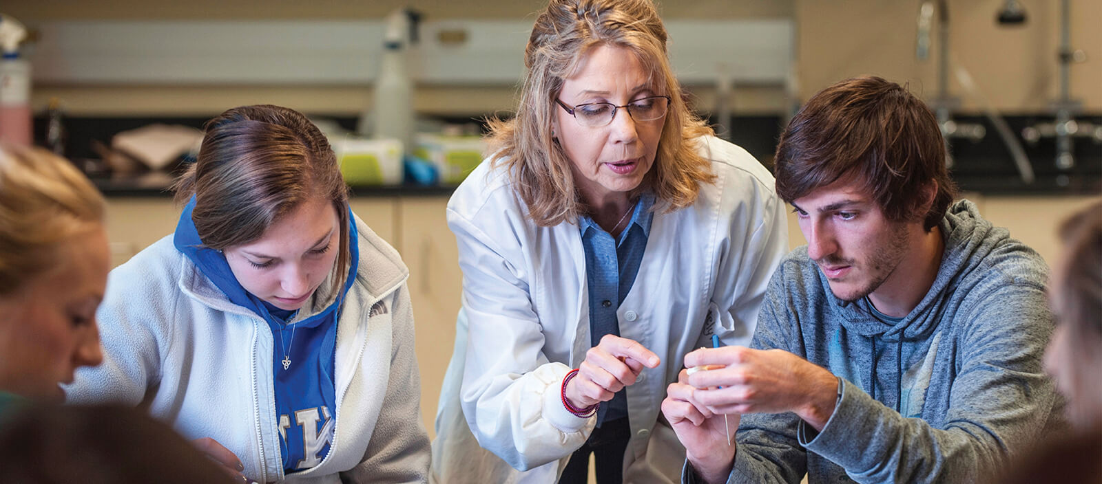 A science faculty member helps two students during a lab.