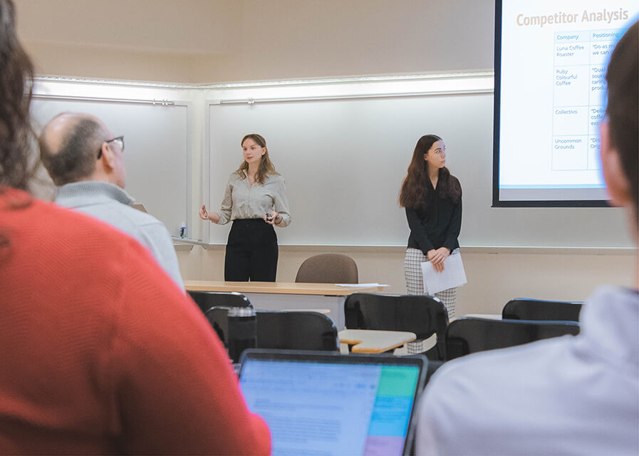 Two female students present to a room of area professionals.