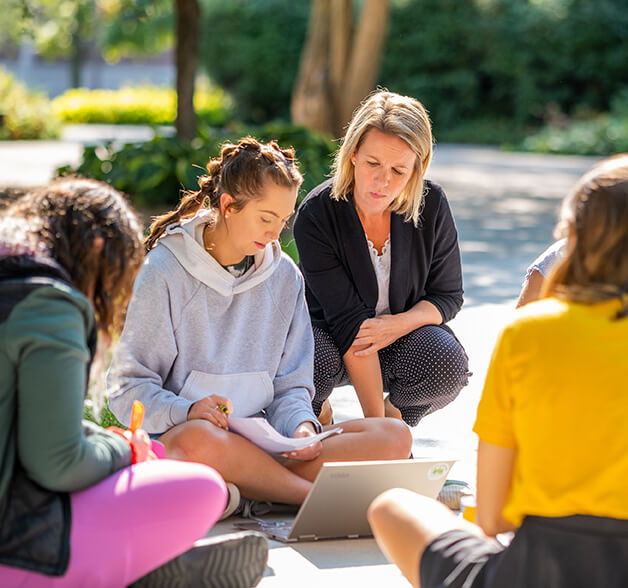 Students work together in a group outside with their professor