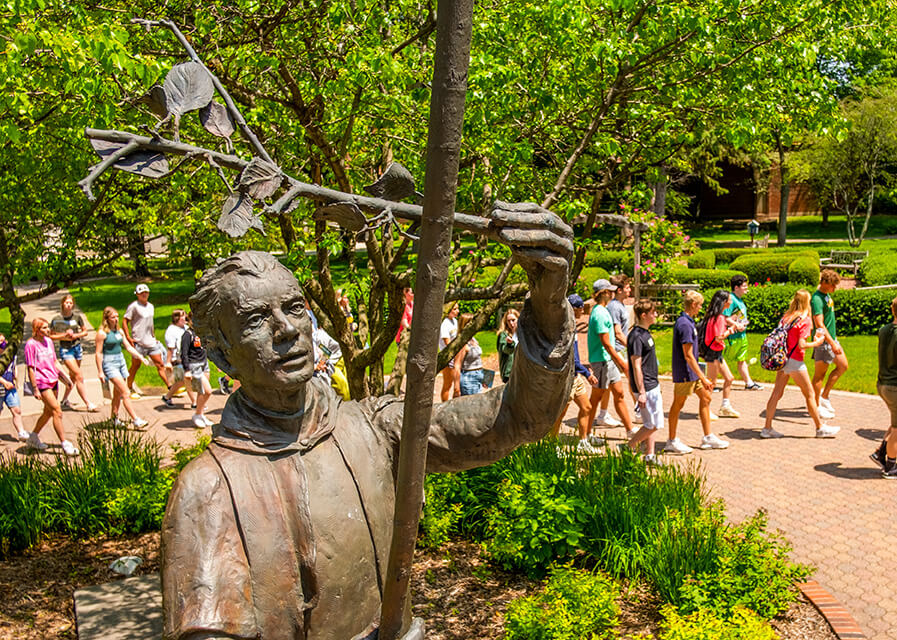 Students walk behind a statue of St. Norbert