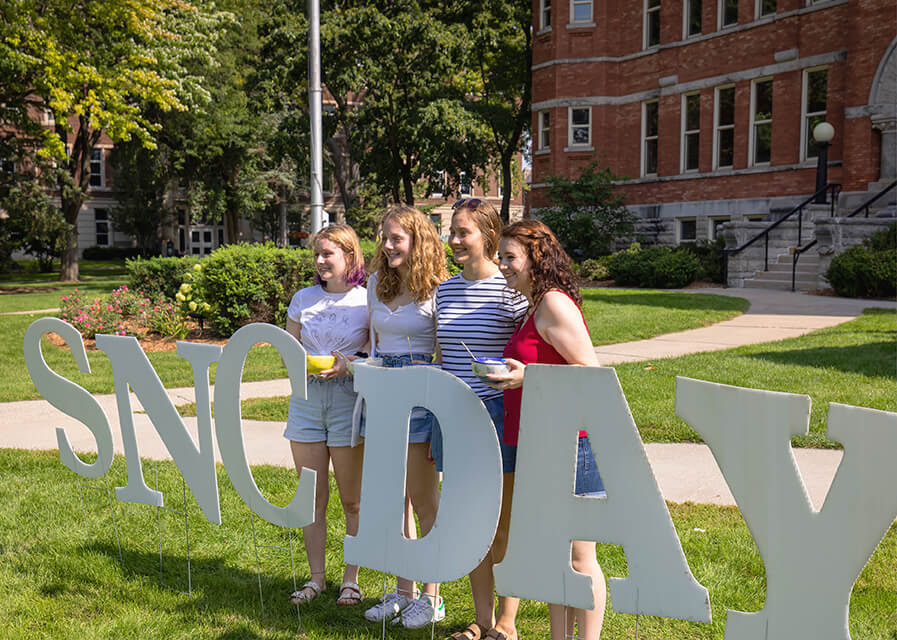 Students pose to take a picture behind the SNC day sign
