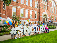 family poses for a photo with a SNC Day sign outside of Main Hall