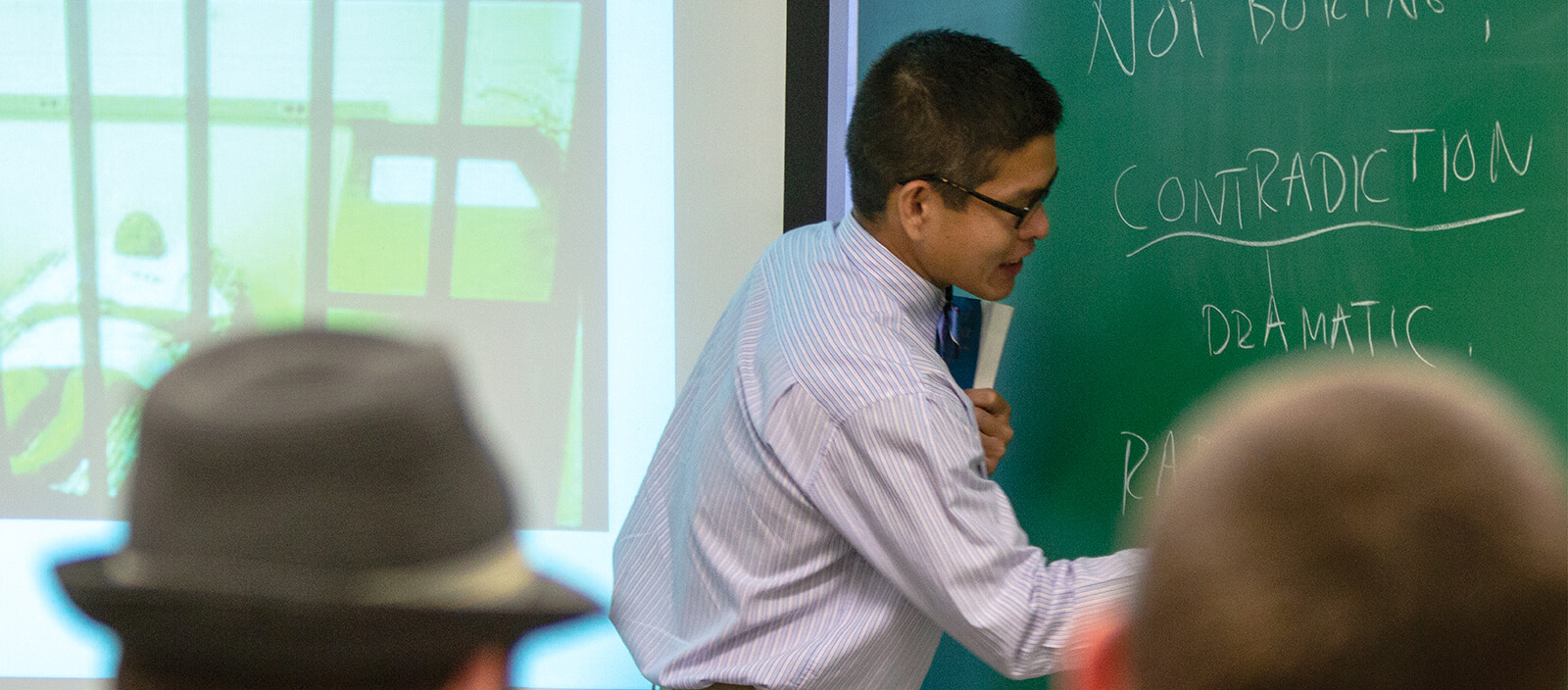 Professor Ben Chan writing on a chalk board in a classroom.