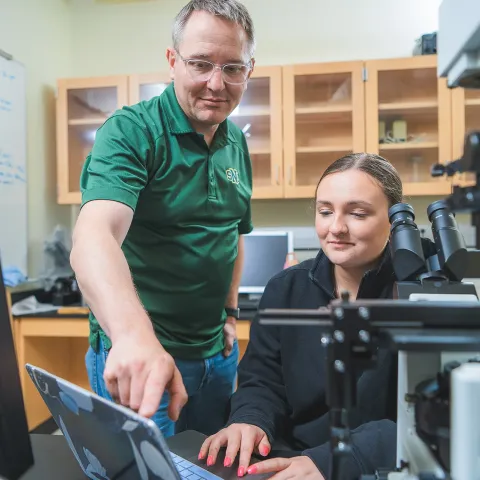 A male faculty member is pointing to a data point on a screen for a student