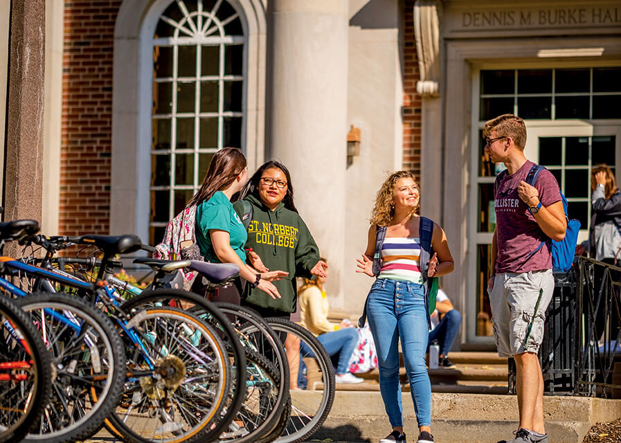 Students stand and talk by a bike rack outside of a campus residence hall